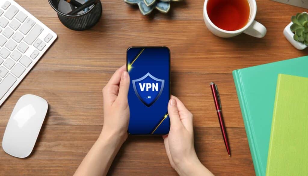 Ein Desktop mit jemandem, der ein Mobiltelefon mit VPN-Schild-Logo hält