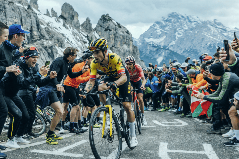 Professional cyclists pedal in the mountains during a race while being cheered on by fans.
