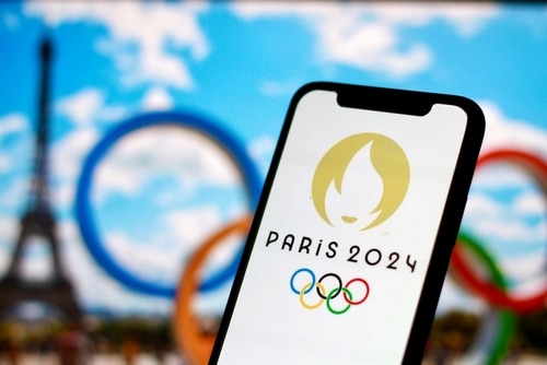 Telefono con il logo delle Olimpiadi in primo piano e i cerchi olimpici e la Torre Eiffel sfocati sullo sfondo
